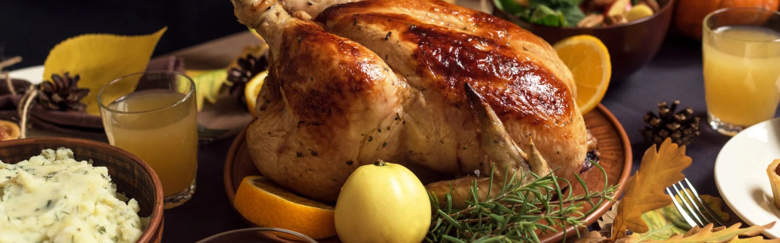 Golden roasted turkey on a platter garnished with rosemary, apple, orange slices, and mashed potatoes.